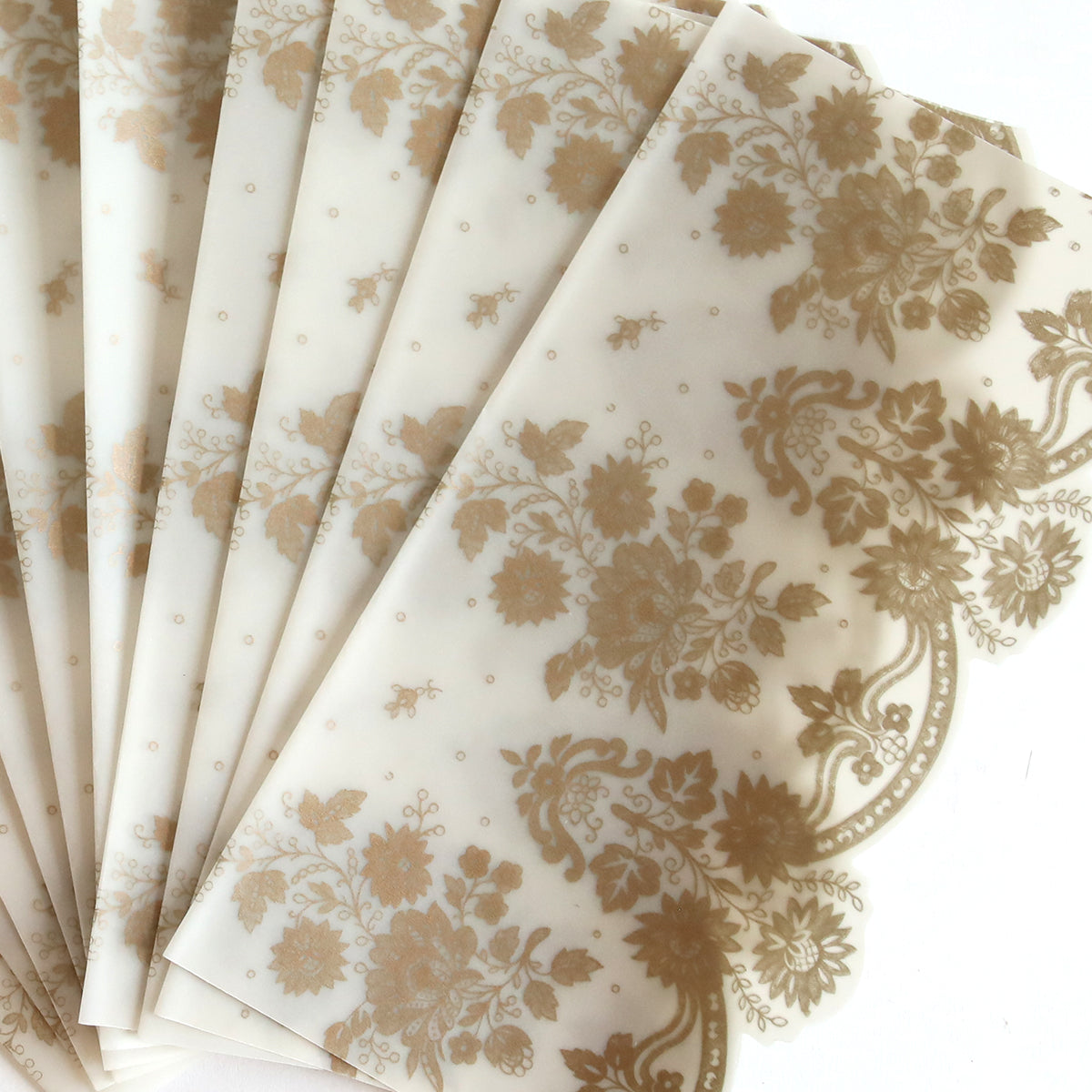 The Gold Vellum Side Wrap 10 pack includes semi-transparent wraps with gold floral designs, ideal for wedding invitations, beautifully fanned out on a white surface.