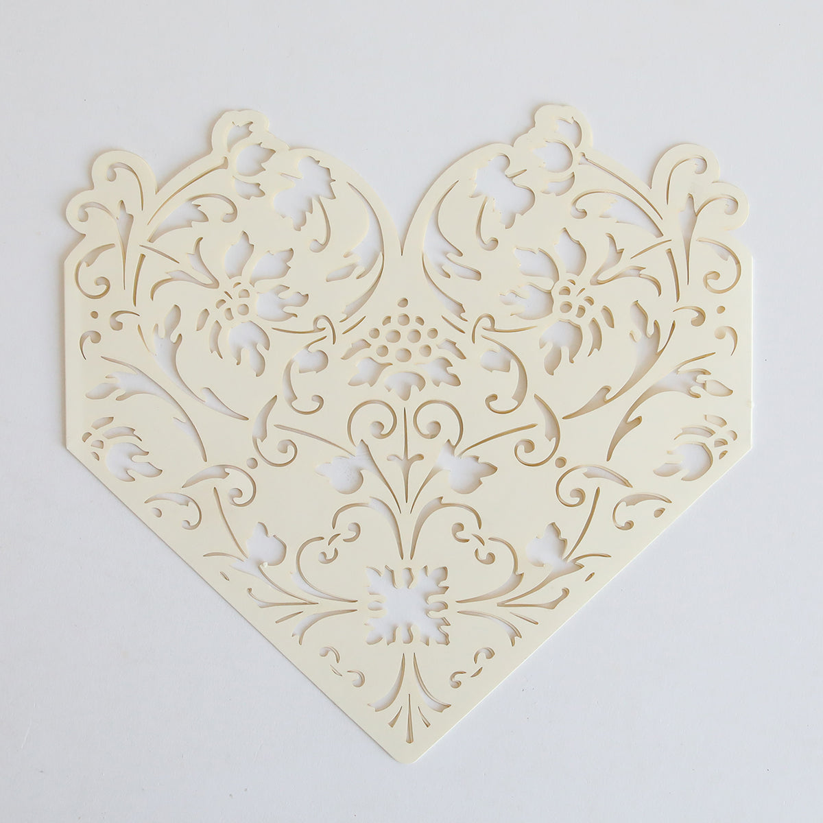 The Ivory Diecut Heart Sleeve 10 pack features intricately cut, cream-colored sleeves with a symmetrical floral heart design, perfect for elegant wedding invitations. Set of 10, shown on a plain white background.