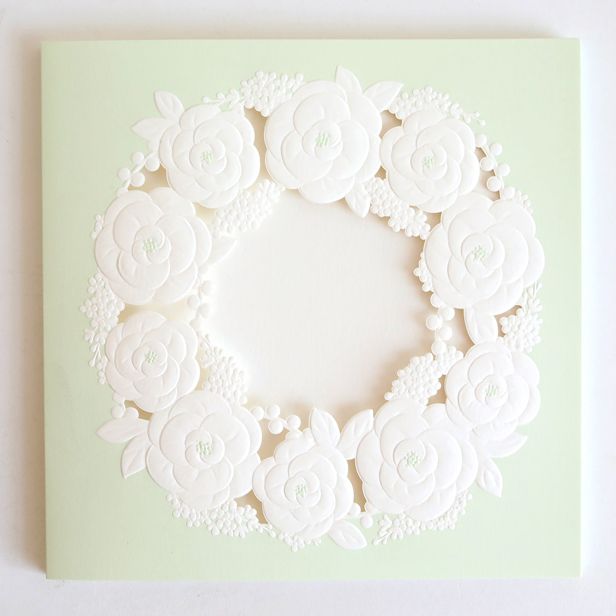 The Floral Wreath Laser Cut Square 10 pack features pale green square cards with a detailed, white embossed floral wreath in the center, perfect for custom invitations.