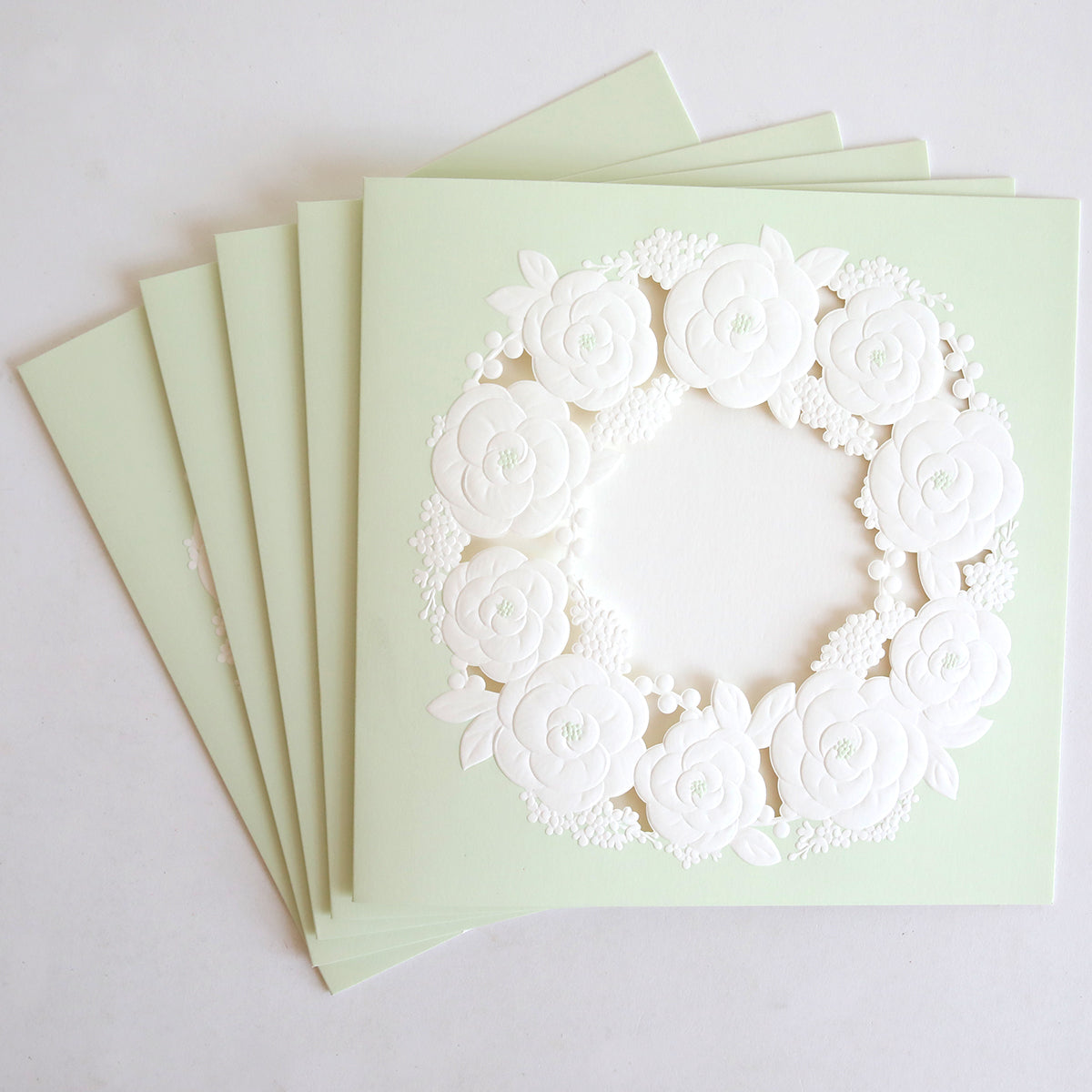 The Floral Wreath Laser Cut Square 10 pack features light green cards with an intricate white floral wreath cutout—ideal for custom invitation kits or unique wedding invitations.