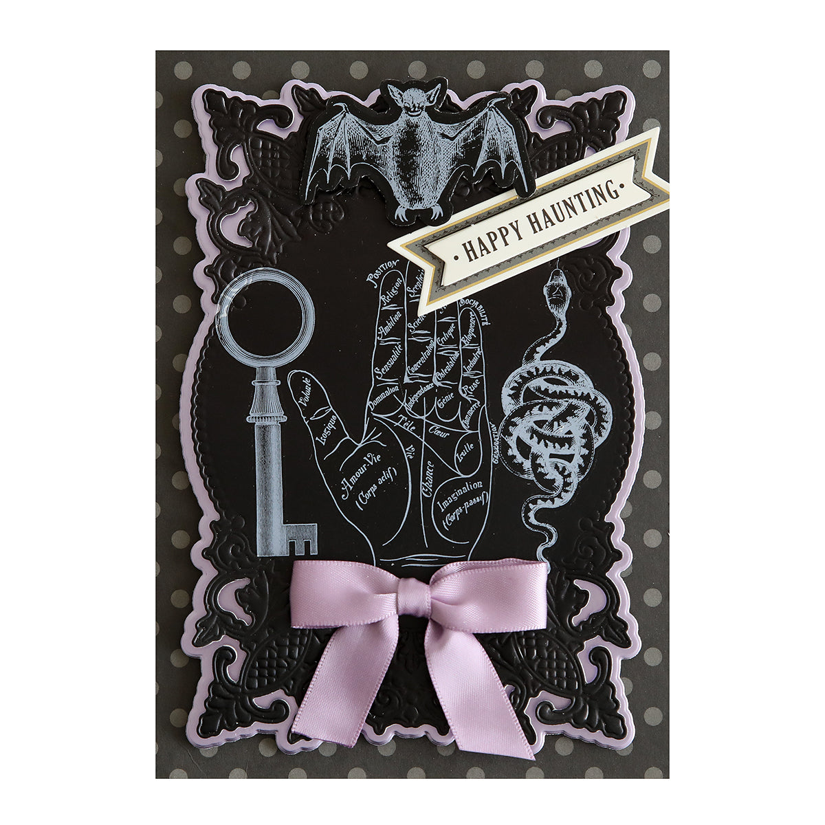 A handmade Halloween-themed card, creatively adorned with illustrations of a bat, key, palmistry hand, and snake, a pink ribbon accentuating the design, and a "Happy Haunting" banner - all heightened with Scary White Rub On Transfers for an extra spooky touch.