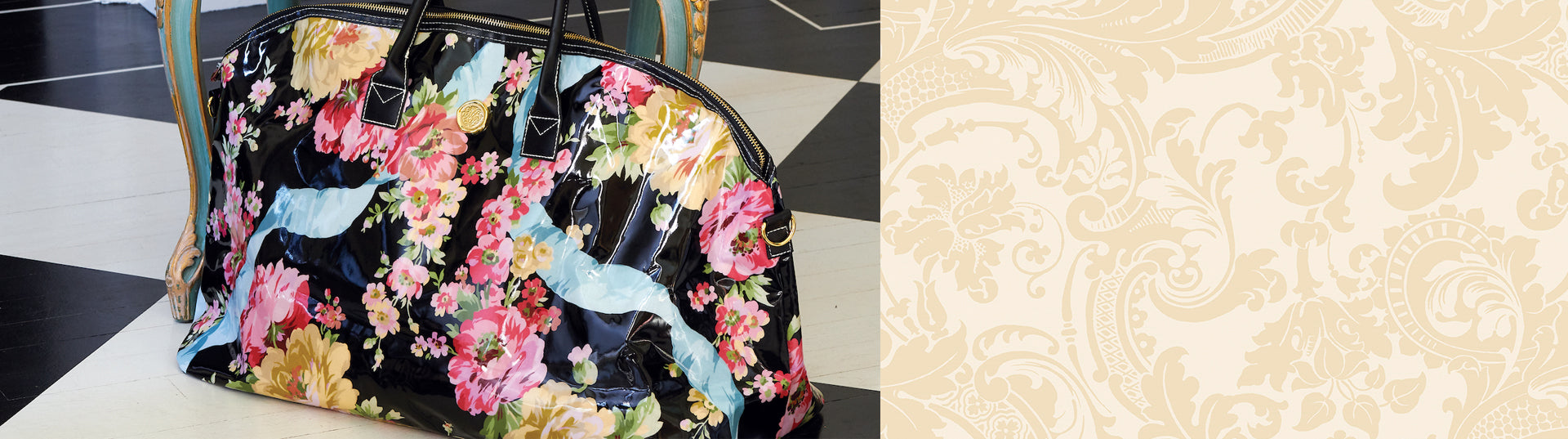 A large, glossy floral-patterned bag with black handles sits on the floor in front of an ornate, upholstered chair.
