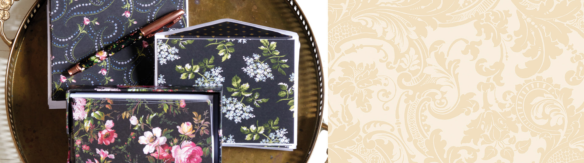 A collection of floral-themed stationery with envelopes and notecards, accompanied by a floral-patterned pen, all set on a gold surface.