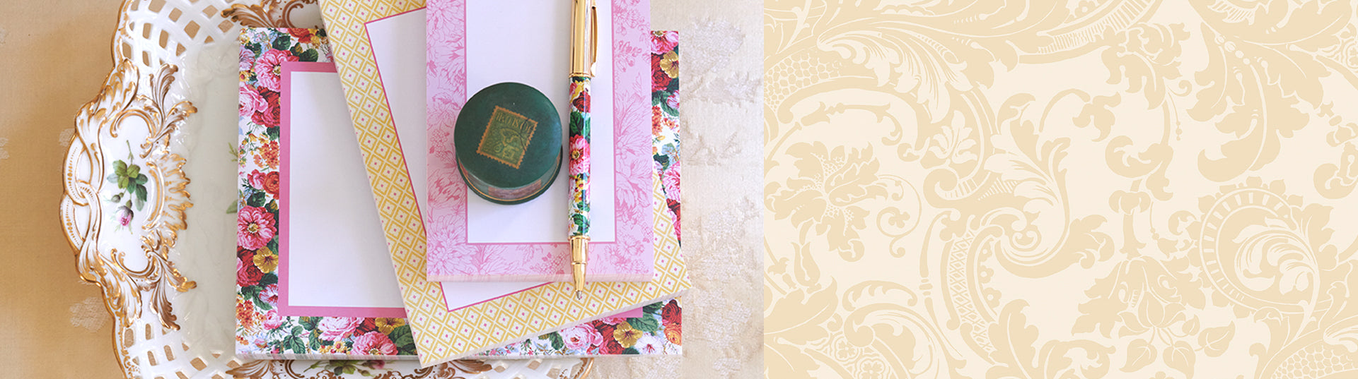 Three floral-patterned stationery sets with matching envelopes, a pen, and a round green ink jar are arranged on a white surface.