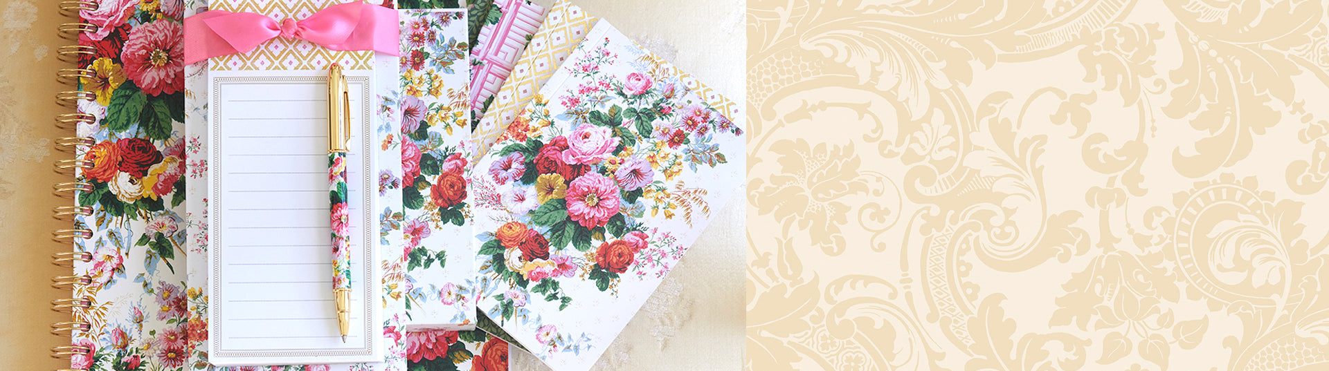 A floral-patterned notepad with a decorative pink ribbon and a matching floral pen placed on a background of assorted floral stationery.