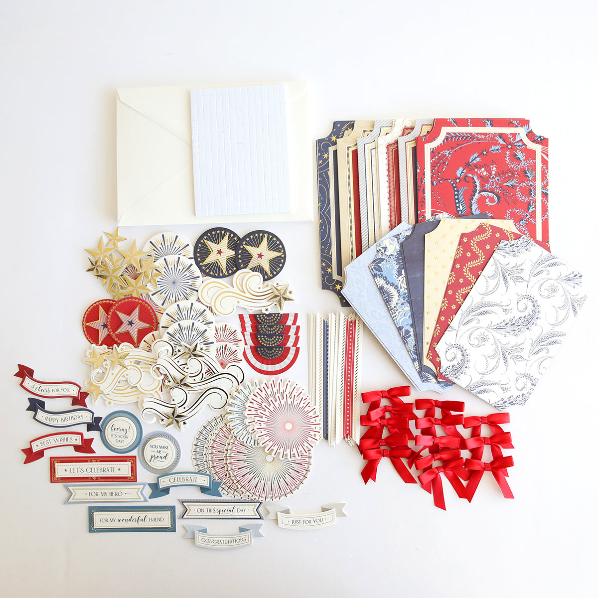 The Simply Celebration Chest Card Making Kit is shown on a white surface with envelopes, patterned cards, decorative cutouts, printed phrases, gold stars, red ribbon bows, and 3D embellishments for creating dimensional cards.
