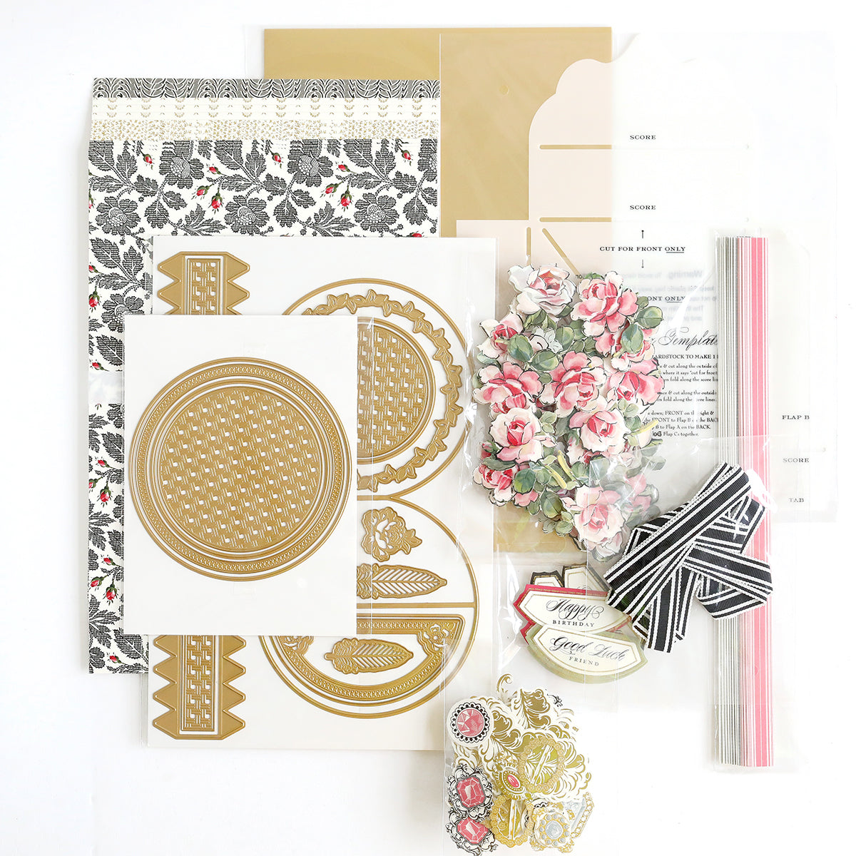 A collection of crafting materials, including floral patterns, gold and white decorative cutouts, striped ribbons, and printed paper, arranged on a white background.