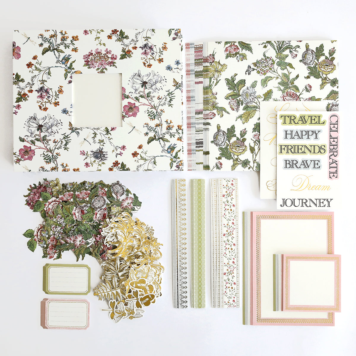 Assorted scrapbooking kit materials including patterned papers, stickers, frames with floral and travel motifs, and journaling tags are included in the Wildflower Meadow Mini Album.