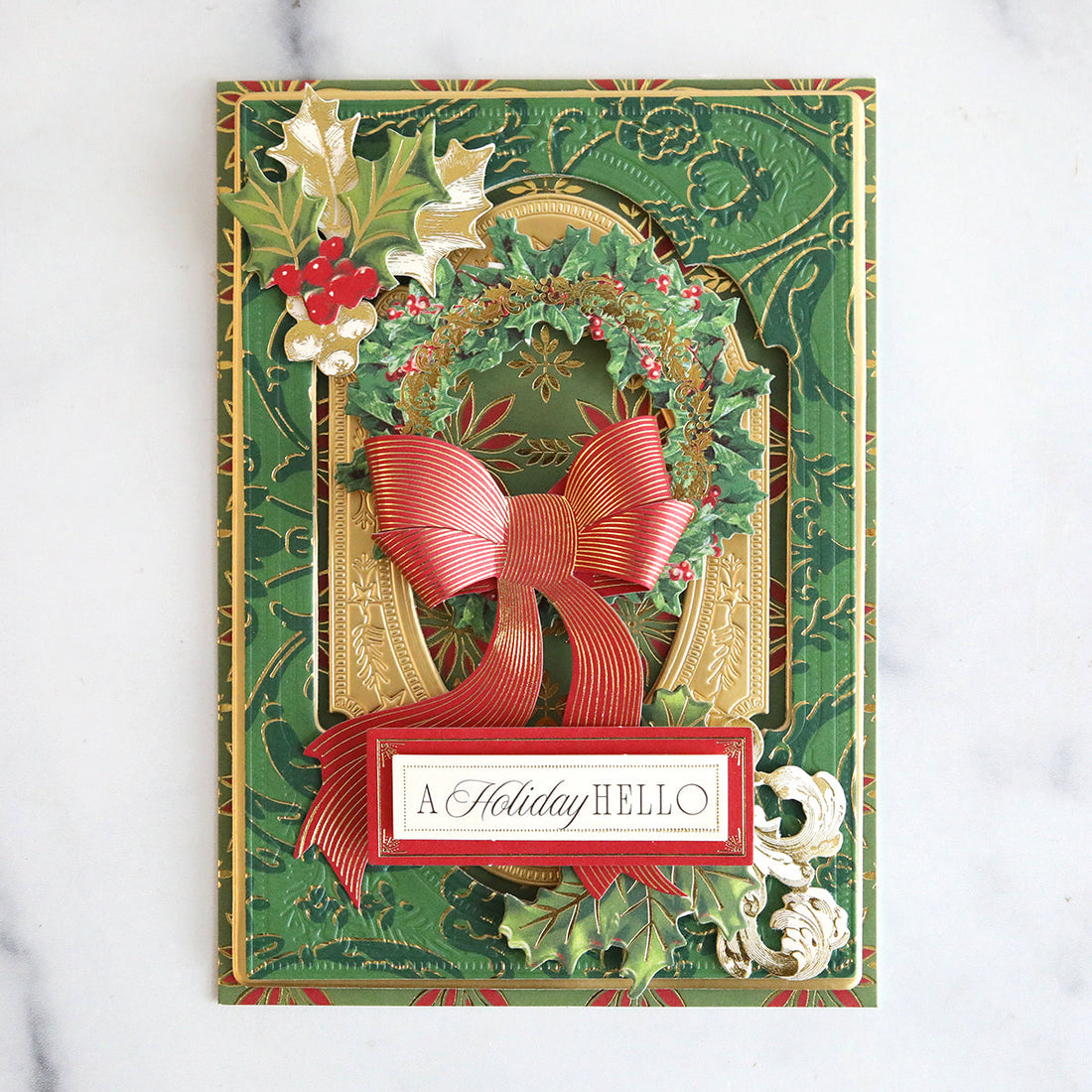 Green festive card with gold foil details, holly and a red paper bow.