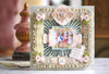 A decorative, floral scrapbook page features a family photo at the center surrounded by intricate paper embellishments, lace patterns, and a butterfly motif.