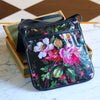 A black purse with flowers on it sits on top of a marble table.