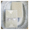 Two ornate white invitation cards, one with a ribbon and intricate lace design, placed on a patterned plate.