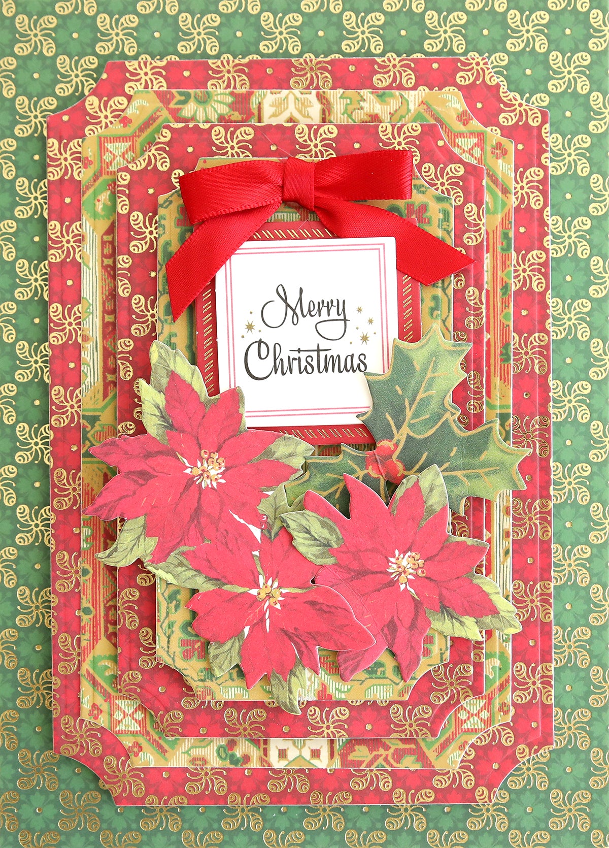 A Christmas card featuring poinsettias, holly leaves, a red bow, and "Merry Christmas" text on a layered red and green patterned background, beautifully accented with festive embellishments and patterned cardstock from the Jasmine Holiday Papercrafting Kit.