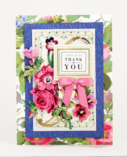 A floral thank you card, created with the Beautiful Botanical Bundle, is perfect for layered card making and showcases layered pink flowers, green leaves, a pink bow, and a framed message that reads “A NOTE TO SAY THANK YOU,” set against a blue and floral background. The elegant design is inspired by antique botanical rub on transfers.
