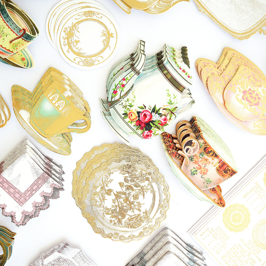 A collection of 120 Favorite Tea Embellishments, featuring assorted vintage-style paper cutouts of teapots, teacups, saucers, and lace doilies, is arranged on a white surface—creating charming sticker accents perfect for handmade cards or as antique tea stickers for all your crafts.