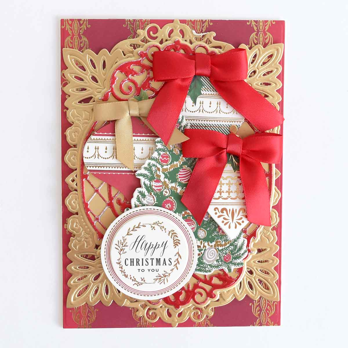 A Reason for the Season Sticker Bundle layered holiday card with gold die-cut flourishes, a Christmas tree, two red ribbon bows, and a circular tag reading “Happy Christmas to you.”