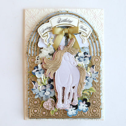 A handcrafted birthday greeting card with a gold and floral design, featuring a central white unicorn motif made using the 3D Unicorn Scene Dies set and a golden "birthday wish" banner, accented by a satin ribbon bow.