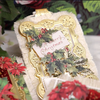 A vintage Christmas card with gold ornate borders and holly leaves, featuring the handwritten message "A Merry Christmas." Red and green floral patterns are visible in the background.
