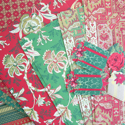 A selection of patterned cardstock in red, green, and gold tones, featuring floral and decorative designs from the Jasmine Holiday Papercrafting Kit—with cut paper tags and festive embellishments, including a charming gift box accent.