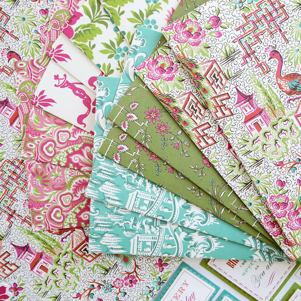 The Chinoiserie Papercrafting Kit with Dies includes assorted patterned sheets featuring botanical, animal, and geometric designs in pink, green, and blue—perfect for scrapbooking or handmade cardmaking projects.