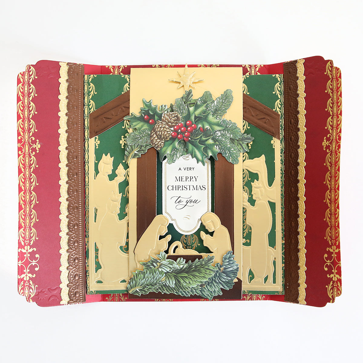 A gatefold Christmas card made with the Nativity Scenes Die Set Collection, featuring a nativity shadow box die-cut layered with holly and pinecones and text reading “A VERY MERRY CHRISTMAS to you.”