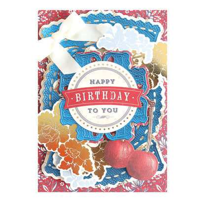 A decorative birthday card on Luxury Matte Foil Cardstock Dark Blue features layered blue, gold, and red designs, gold flowers, two cherries, a white ribbon, elegant embossing, and "Happy Birthday to You" in the center.