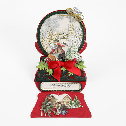 Send warm wishes with a pop-up holiday card inspired by the Snowglobe Easel Card Dies, featuring vintage-style people gathered near a snowy house, intricate winter scenes, a red ribbon accent, and gold snowflake details. Ideal for crafting enthusiasts, this beautifully detailed card reads “Warm Wishes.”.