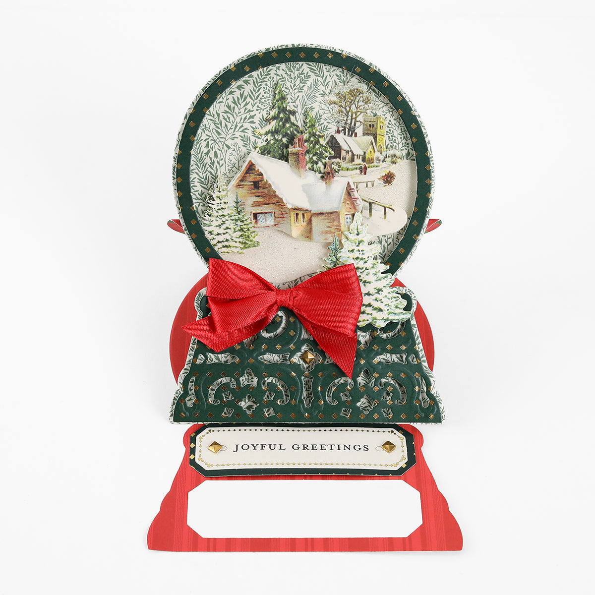 Decorative card featuring a snowy cabin scene, festive green and red accents, a red bow, and “Joyful Greetings” on the front—ideal for crafting enthusiasts. Created with Snowglobe Easel Card Dies and premium metal dies to achieve crisp, detailed accents.