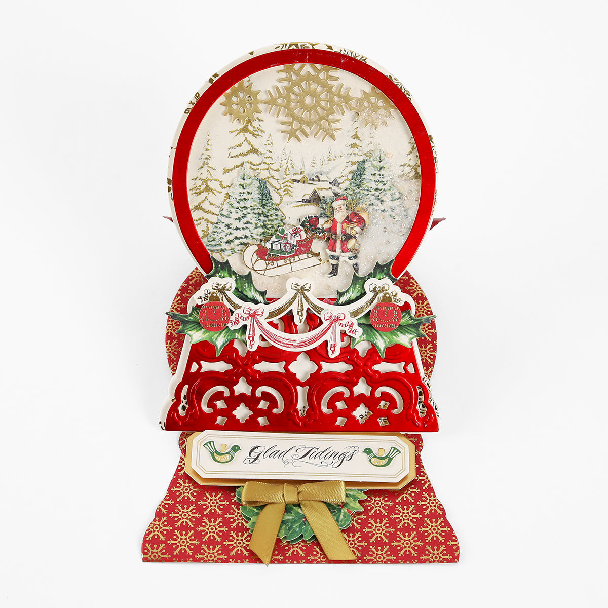 Pop-up holiday card crafted with the Snowglobe Easel Card Dies, featuring Santa in a sleigh amid snowy trees for added detail, adorned with “Glad Tidings” text and ornate red and gold decorative elements.