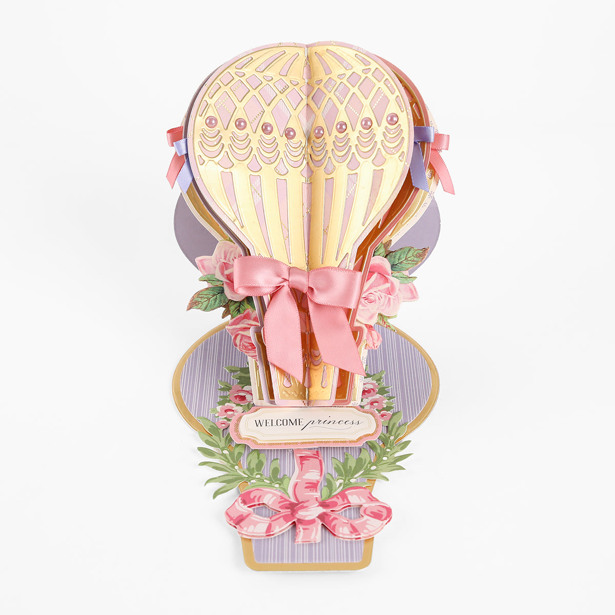 Create standout handmade cards with the Hot Air Balloon Easel Die—a 3D pop-up card featuring a gold and pink hot air balloon, beautifully accented with ribbons, flowers, and a “Welcome princess” sign on a decorative pastel background.