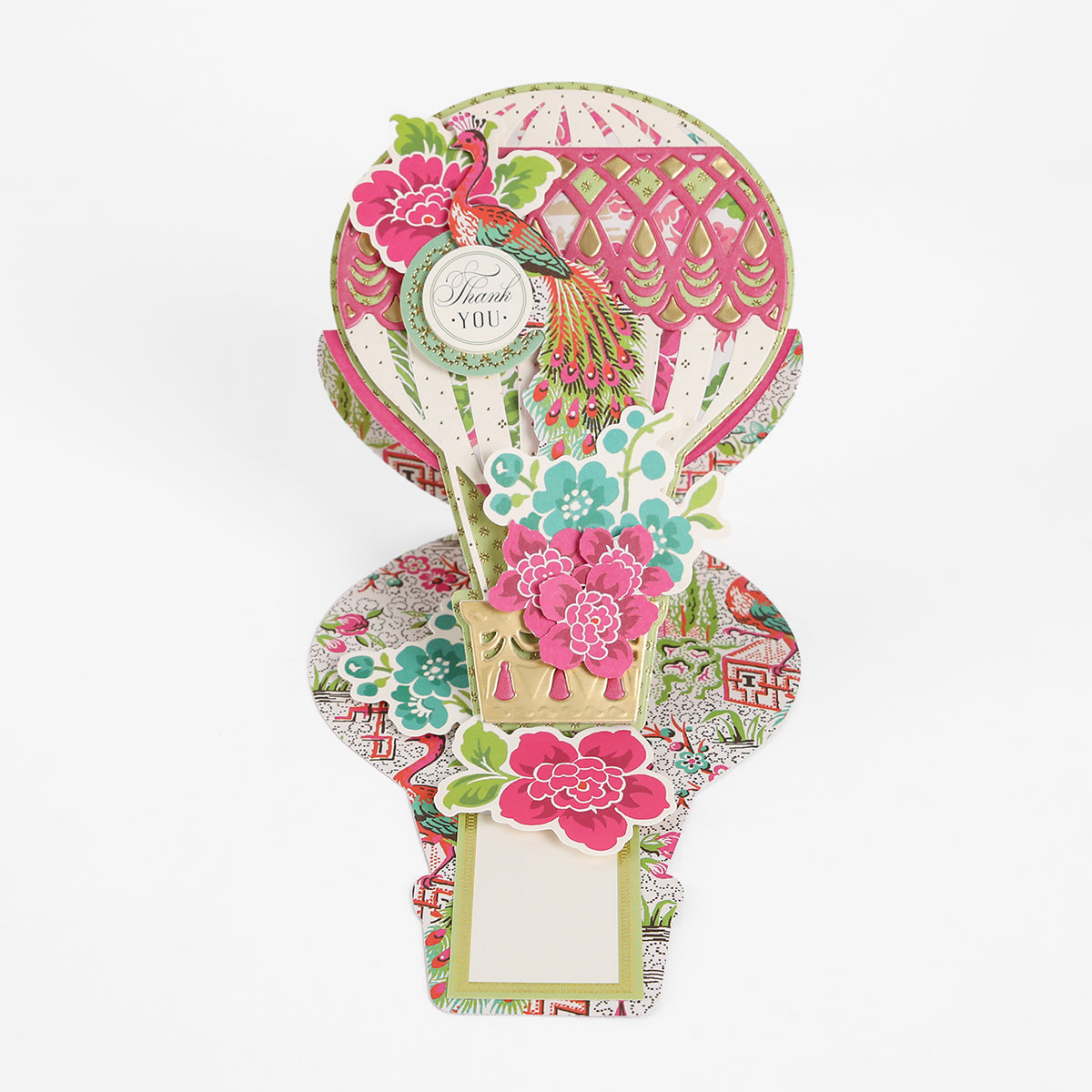 Showcase your handmade cards with the Hot Air Balloon Easel Die, which lets you create a pop-up card featuring a vibrant hot air balloon adorned with floral decorations, a peacock, and a “Thank You” sign set on an elegant patterned base.