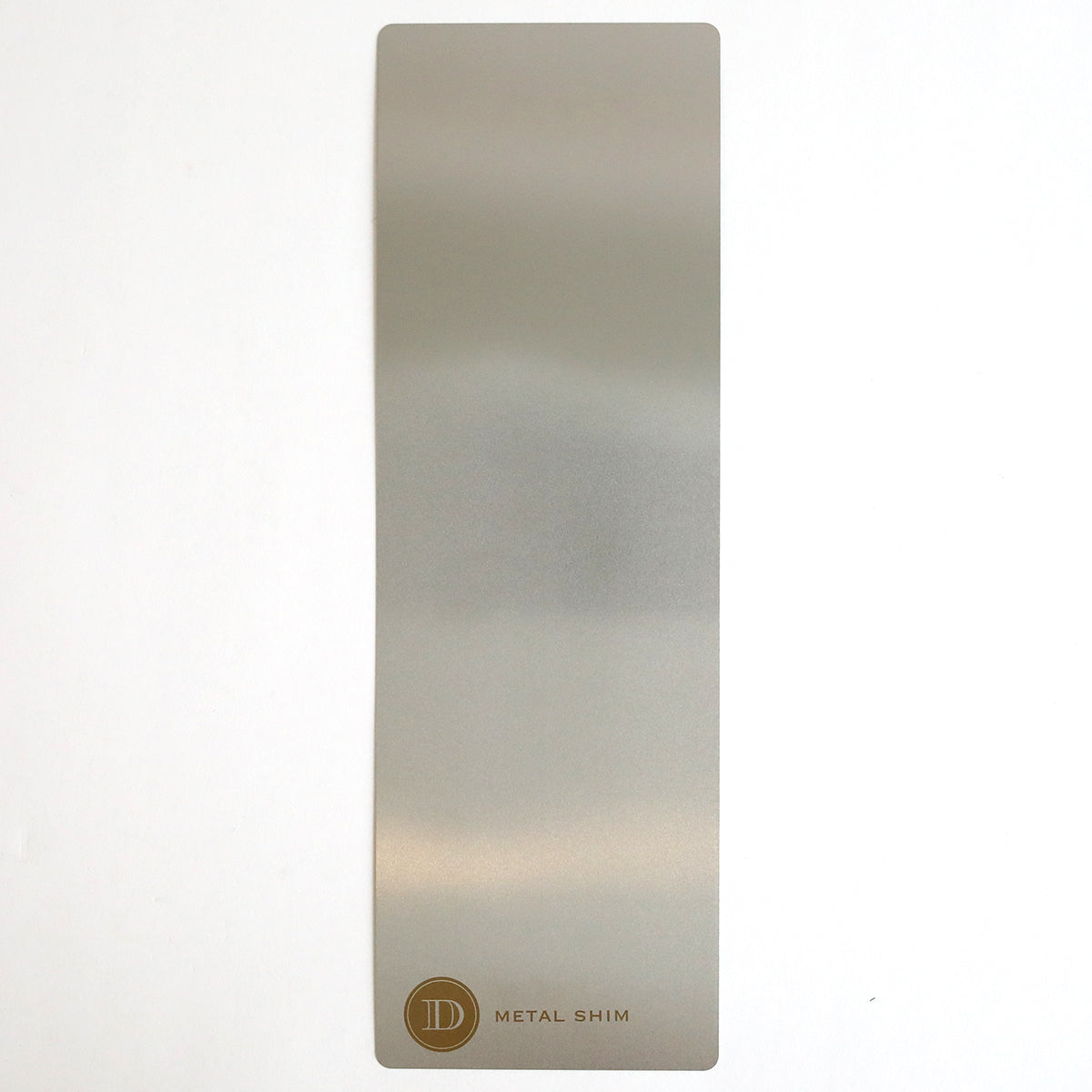 A rectangular metal shim with a matte finish lies flat on a white surface. In one corner, the gold circular logo and “METAL SHIM” text are visible—an ideal accessory for embossing or die cutting with the Empress Mini 13" Full Plate Set.