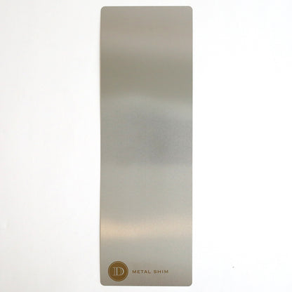 A rectangular metal shim with a matte finish lies flat on a white surface. In one corner, the gold circular logo and “METAL SHIM” text are visible—an ideal accessory for embossing or die cutting with the Empress Mini 13" Full Plate Set.