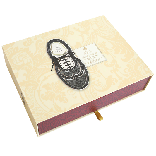 A Paper Wingtips Finishing School Craft Box with a black dress shoe illustration and a Paper Wingtips label on the lid. The box features a light yellow and white patterned design with a red side and a small handle at the bottom.