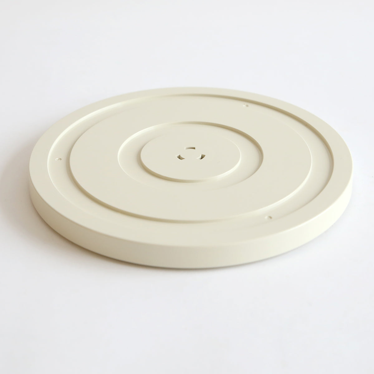 An off-white, round, flat plastic disc with a central indention and small holes, likely a part from the Empress Elite Machine with Large and 13" Plates, is shown on a plain white surface.