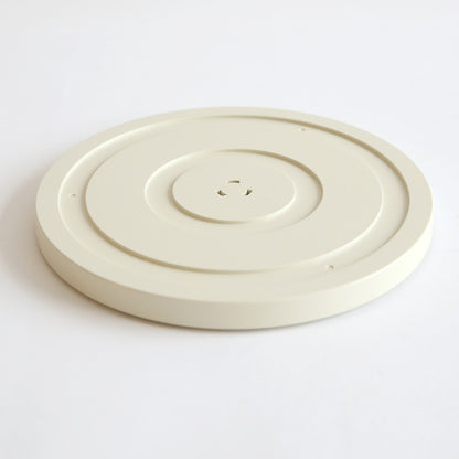 An off-white, round, flat plastic disc with a central indention and small holes, likely a part from the Empress Elite Machine with Large and 13" Plates, is shown on a plain white surface.