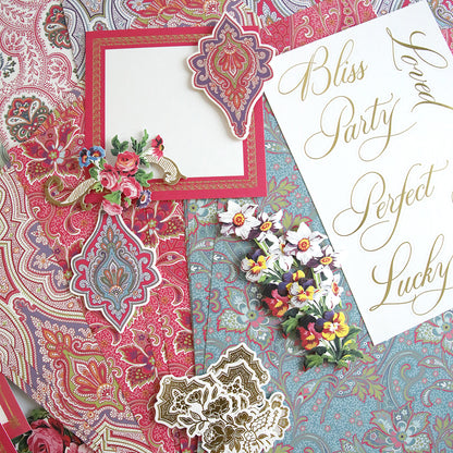 The "Paisley Papers and Embellishments" collection features vibrant paisley and floral patterned scrapbook pages adorned with gold calligraphy words such as "Bliss" and "Perfect," along with a variety of elegantly arranged embellishments.