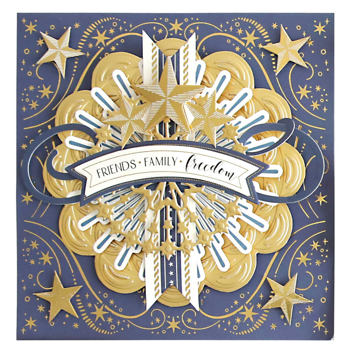 The Celebration Chest Craft Box Card Kit includes an elegant card adorned with a gold and navy design, featuring foil accents in stars and a banner that reads "Friends • Family • Freedom." The card's decorative appeal is further enhanced by swirling patterns and layered elements reminiscent of star-studded cards.