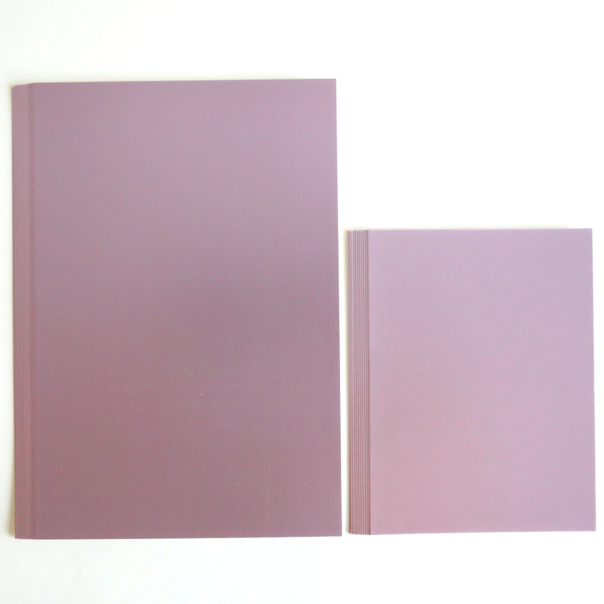 Two closed Luxury Matte Foil Cardstock Lavender notepads rest on a white surface. The larger and smaller ones both feature plain pastel covers with subtle elegance.