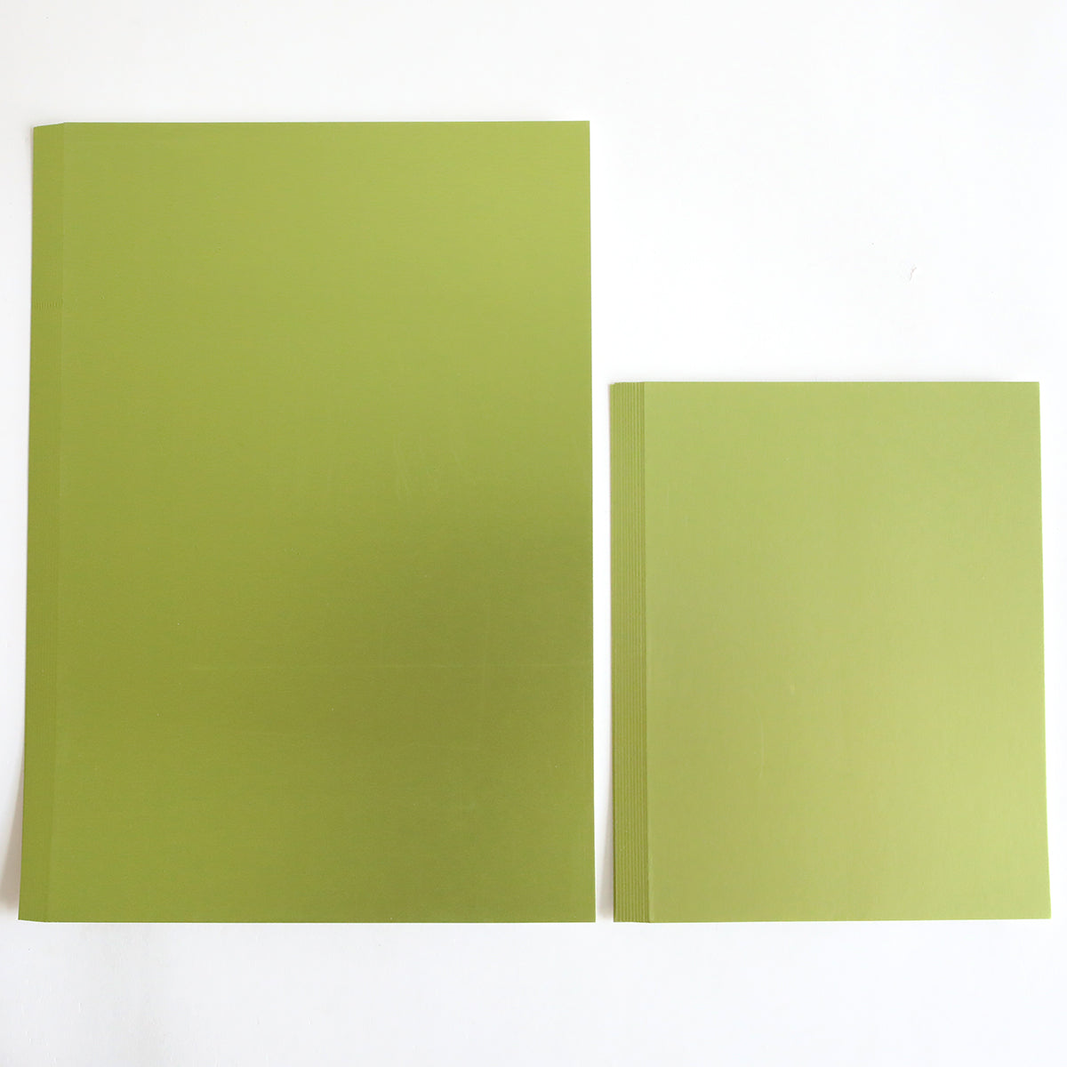 Two green books rest on a white surface; the larger one on the left, resembling Luxury Matte Foil Cardstock Green, stands next to the intricately detailed one on the right.