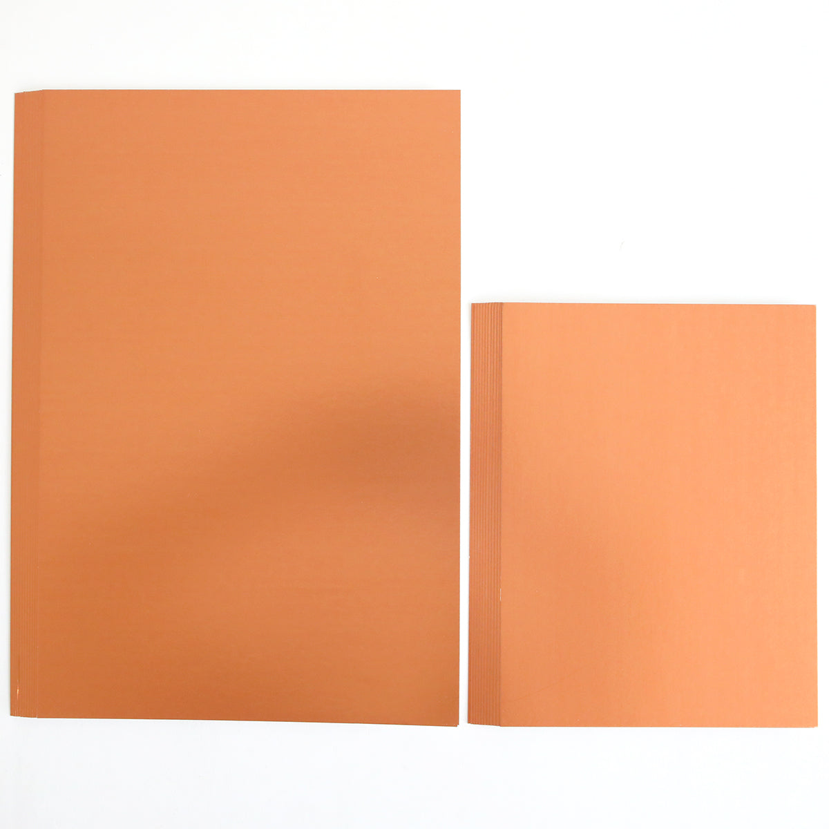 Two stacks of orange paper are placed side by side on a white surface; the left stack is larger and rectangular, while the right stack is smaller and square—perfect for creating your own Haunted Halloween Haul or adding festive flair with stickers and glitter cardstock.