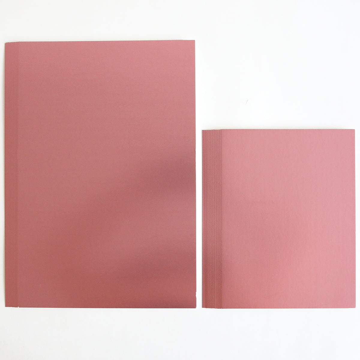 Two stacks of Luxury Matte Foil Cardstock Pink are placed side by side on a white surface; one stack is larger and one is smaller—ideal for diecutting projects.