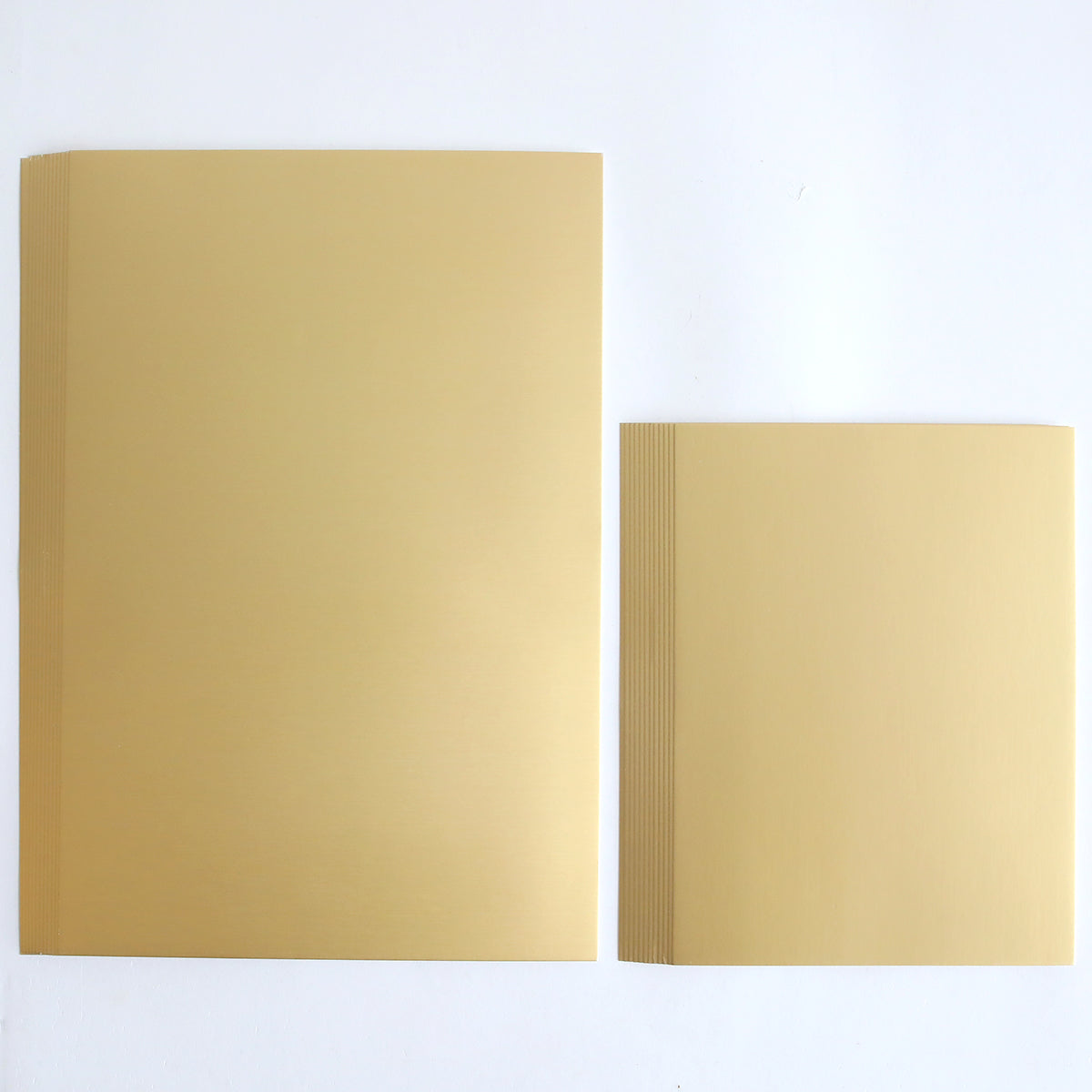 Two stacks of Luxury Matte Foil Cardstock Gold rest on a white background, with the left stack noticeably larger than the right, making it an ideal choice for diecutting projects.