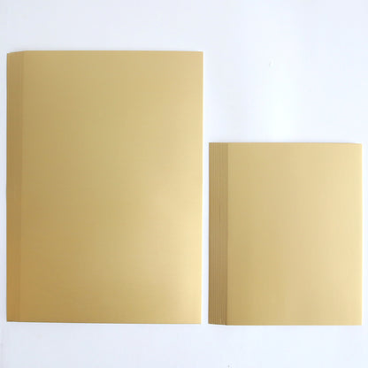 Two stacks of Luxury Matte Foil Cardstock Gold rest on a white background, with the left stack noticeably larger than the right, making it an ideal choice for diecutting projects.