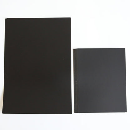Two stacks of Luxury Matte Foil Cardstock Black sheets—ideal for embossing or die cutting—are displayed on a white surface, with the larger stack on the left and a smaller one on the right.
