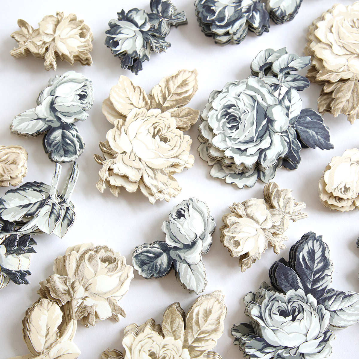 A collection of intricately designed Black and Cream Flower Stickers, featuring shades of white, cream, and gray with detailed leaves and varying levels of shading, are scattered on a white surface—perfect embellishments for scrapbook pages.