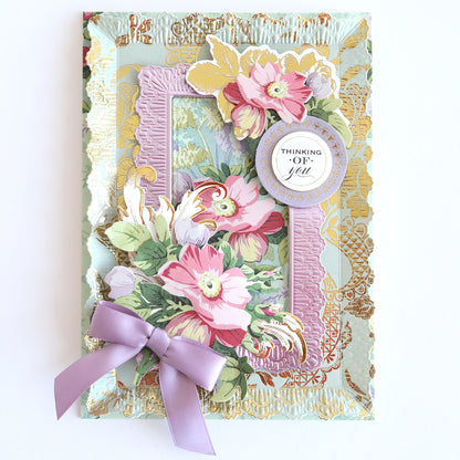 The Floral Paper Anthology card is crafted from floral cardstock with layered designs, featuring a "Thinking of You" message and a purple ribbon bow. Ideal for scrapbooks or as an elegant handmade card.