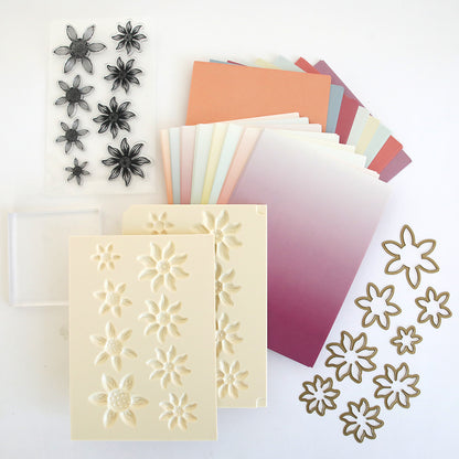 The Blooms Flower Mold, Stamps and Dies set features flower stamps, colored cardstock, floral embossing folders, a shaping mold, and metal cutting dies—all arranged on a white surface.
