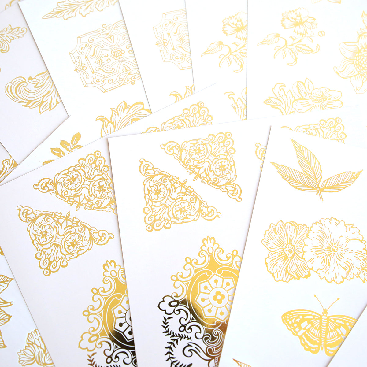 The Glorious Foil Rub Ons Gold collection includes white cards with intricate gold designs, like floral motifs, butterflies, and abstract patterns—ideal for craft projects using gold foil transfers.