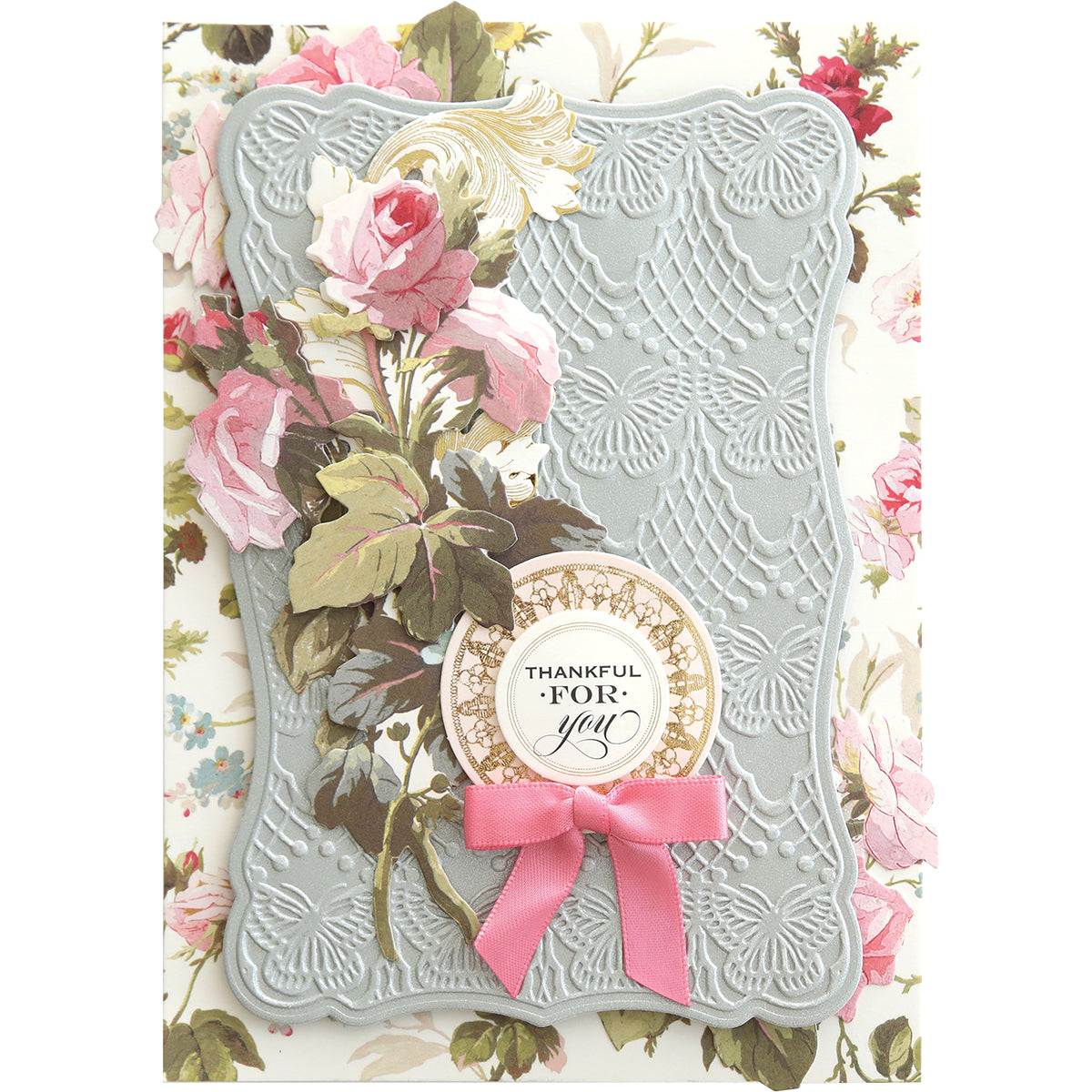 The Butterfly Pattern Cut & Emboss Folders create an elegant card with embossed floral designs, featuring pink roses and a "Thankful for You" message on a circular plaque adorned with a pink bow. Ideal for scrapbook pages, they add charm with delicate butterflies.